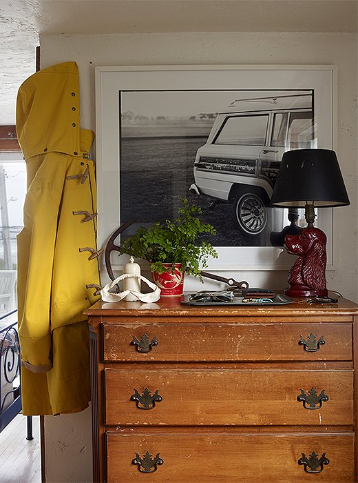 In the bedroom, a lamp made from a ceramic bust of a spaniel sits atop a Federal-style dresser in front of one of Matt’s photographs. The classic yellow raincoat is also his. 
