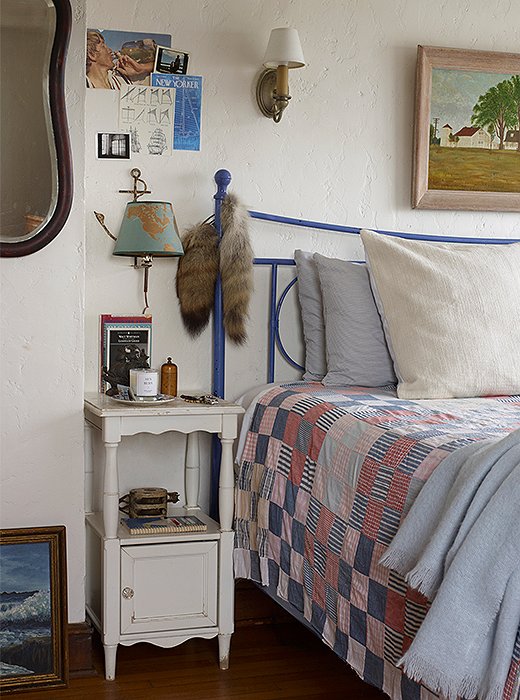 Beside a bed frame sits a nightstand unencumbered by a table lamp. Instead, a brass sconce shaped like a fishing lure was hung, making the most of a spare space on the white plaster wall. 
 
