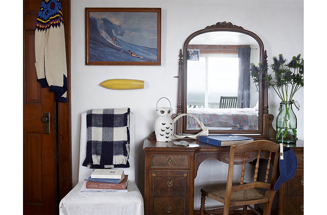 A Queene Anne dressing table is paired with a spindle-back chair and a ceramic owl. A print from yesteryear depicting two surfers hangs next to the closet door draped in Fair Isle. 
