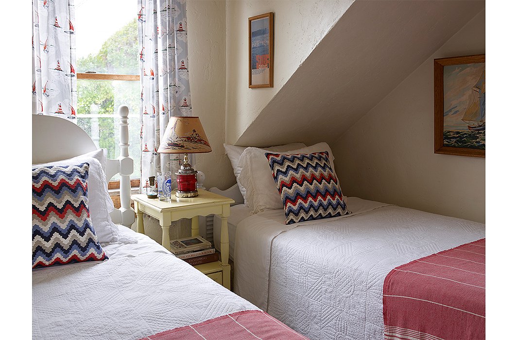 The cheery guest room features twin beds and a ship light-turned-lamp shaded by a coastal scene. Quilts, in lieu of duvets, are in line with Matt’s affinity for handcrafted things. 
