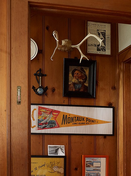 At the bottom of a staircase hangs a captain’s portrait, a pair of antlers, and a framed Montauk flag. 
