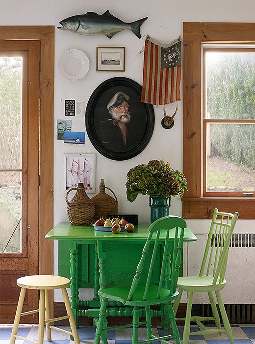Surrounded by mismatched chairs, the well-used table in Williamsburg green is the kitchen’s colorful focal point. Behind, an Americana-inspired gallery wall features yet another captain, an odd plate, and a Revolutionary flag. On the floor, blue-and-white linoleum offers (an original) retro touch. 
