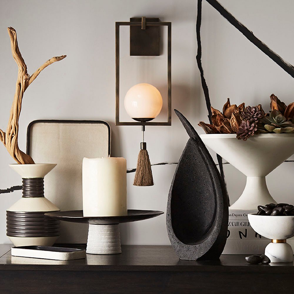 In the center of the above tableau is the Trapeze sconce by Ray Booth in an antique-brass finish. Other pieces include the charcoal Celine sculpture and the concrete Cayden centerpiece (which can also be used as an outdoor planter), and the white marble Tate container.
