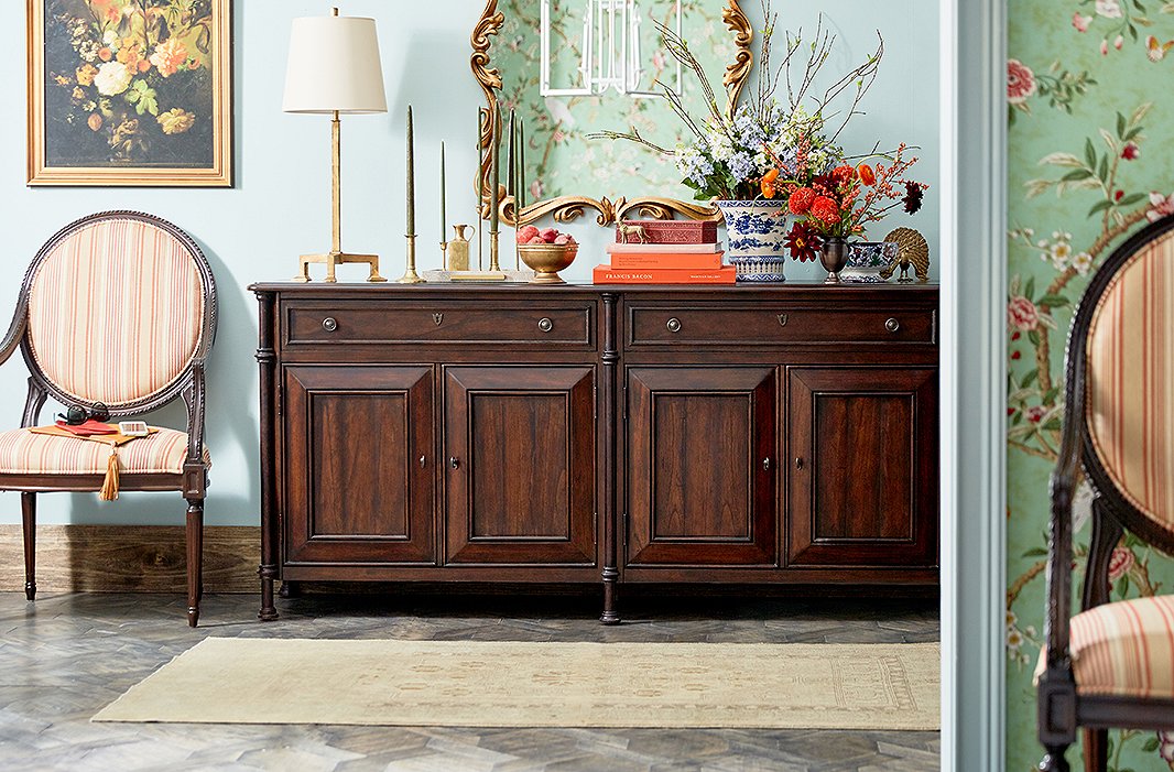Brass candlesticks, a stack of orange books, and flowers in rich autumnal hues give this elegant entryway a sense of seasonality. Photo by Tony Vu.

