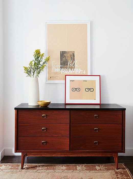 Yesteryear’s nightstands meet their match with a black-top dresser. The Godard | Woody Allen print was Mindy’s own. Note the red frame, which was chosen to contrast with the room’s peachier hues, as seen in the print itself and the Oushak rug below.
