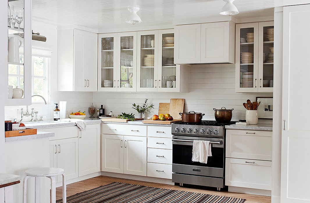 A salt-bag rug from Nepal’s Manang District softens the otherwise all-white kitchen. A library light by Thomas O’Brien for Visual Comfort provides task lighting over the sink, lending the garden view a picturelike quality. 
