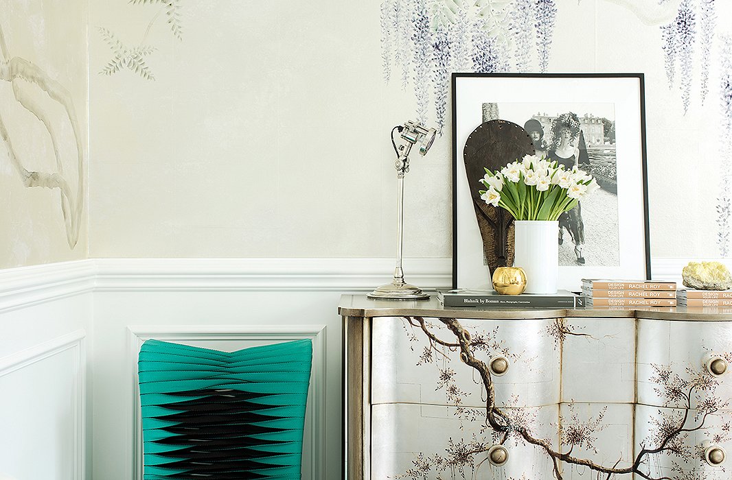 Reiterating her balance of edge and softness, a turquoise chair made from seat belts is placed next to a chest, hand-painted with romantic branching florals that nod to the wallpaper, that holds all of Rachel’s office essentials.
