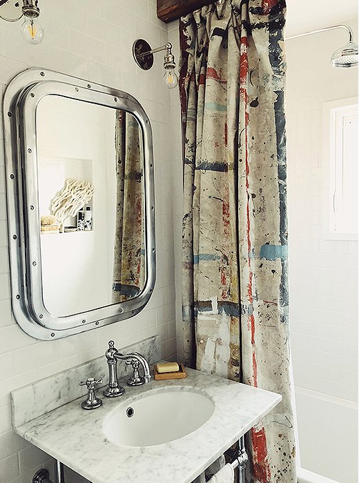 A riveted chrome mirror lends nautical charm to the bathroom, accented with found coral and an artfully paint-splattered shower curtain. White subway tiles keep the look bright and fresh.
