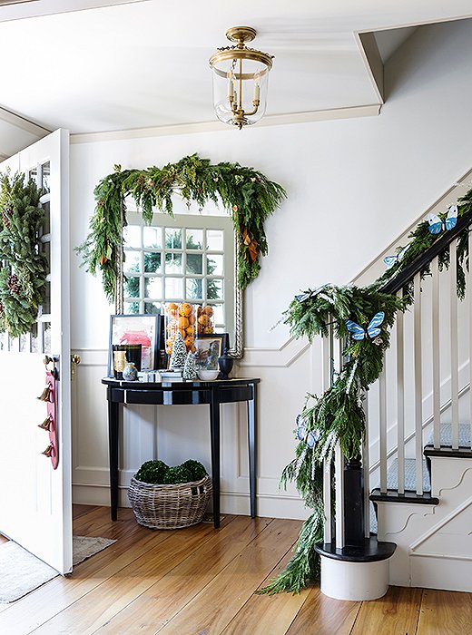 In the foyer, a traditional evergreen garland goes whimsical with a mix of fresh foliage and woodland-inspired trimmings. 

