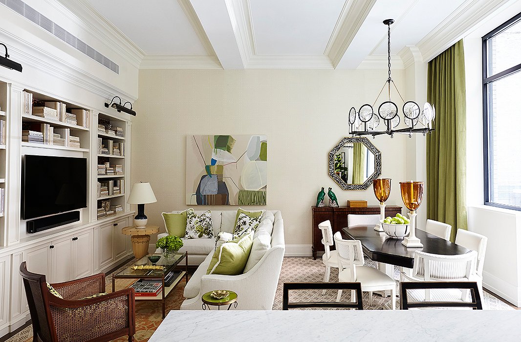 Georgie and Jen freshened the living room walls with a coat of Benjamin Moore’s Acadia White. A scaled-down sectional separates the living and dining areas, while accents of green help unify the open-plan space.
