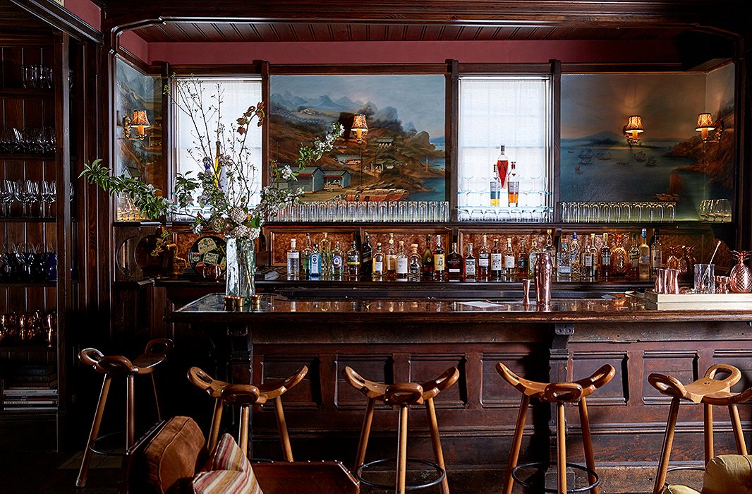 The paneled bar was sourced from the Midwest and topped with a wood-trimmed honed-marble slab. The scenic panels behind the bar, by New York decorative painter Dean Barger, take inspiration from a painting in the Peabody Essex Museum and depict historic Chinese merchant ports.
