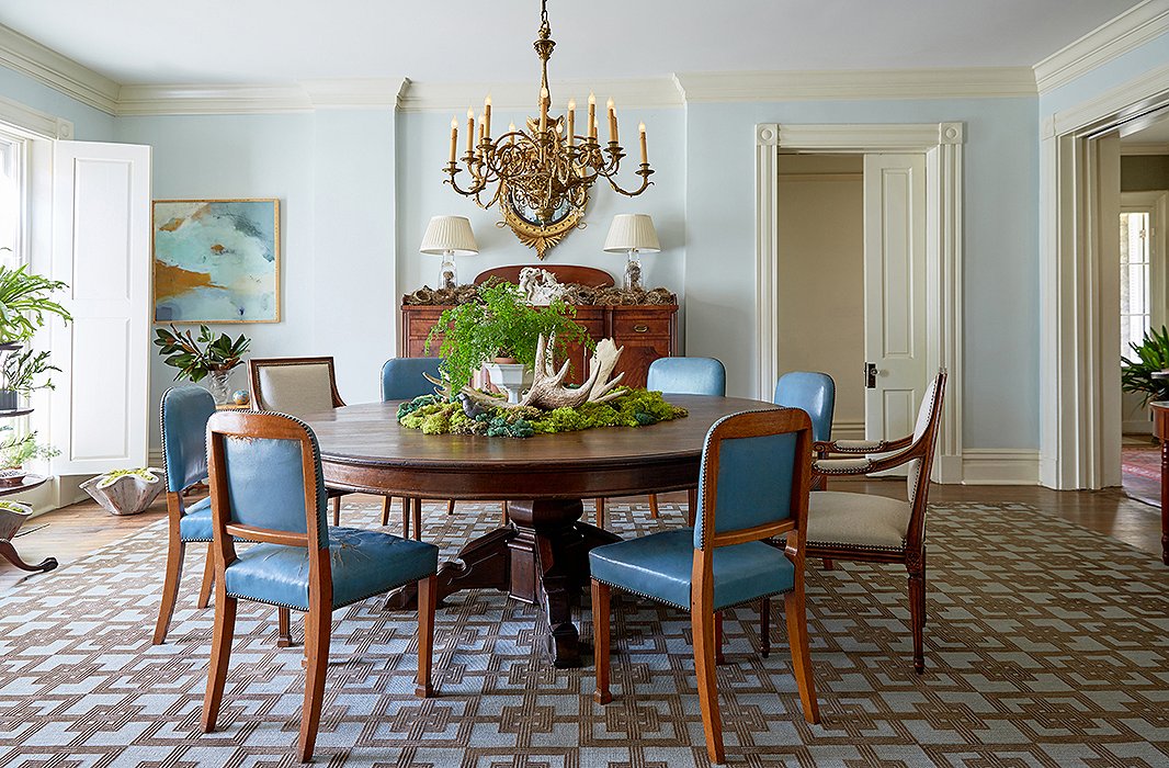 A pedestal table for 12 surrounded by mismatched chairs is centered under a brass chandelier. The centerpiece is changed out seasonally but remains consistently green in warmer months. “Moss, ferns, whatever’s available I tend to use,” Jon says. Behind, a sideboard covered in birds’ nests collected from transplanted trees minimizes any sense of formality.
