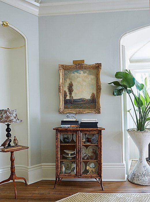 A Brighton-style bamboo cabinet sits beneath an English oil painting. “The art helped inform the room’s wall color,” says Jon, but it was Dale who chose all the swatches. In this case, Sherwin Williams’s Aloof Gray provides a cool contrast to the space’s brassier hues. 
