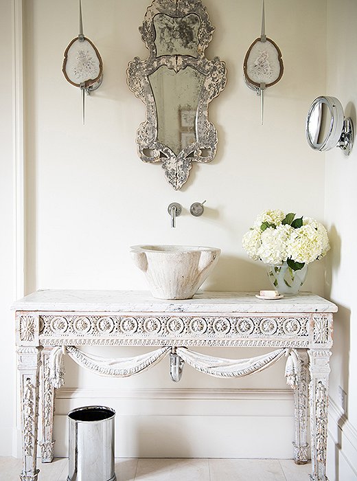 Tara created a bathroom sink to her taste by converting an Italian mortar to a sink and installing it in a white vanity table. A Venetian mirror hangs above it.

