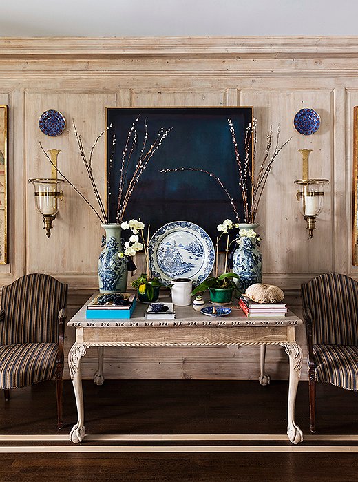 An oak ball-and-claw table matches the light-tone stripes on the stained wood floors, while pieces of blue-and-white pottery pop against an abstract painting in indigo hues. At night, visual romance emanates from flickering candles in the glass hurricane sconces.


