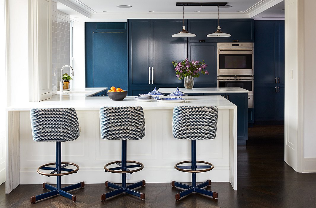 A trio of blue-and-white barstools accented with brass complement the rich navy-blue cabinetry.
