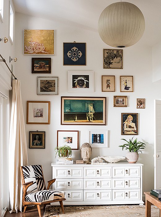 The master bedroom’s gallery wall begins at the top of a lacquered vintage chest and ends at the ceiling. Featured works include a photograph taken by Paula on her honeymoon, gifts from friends, and vintage finds. 
