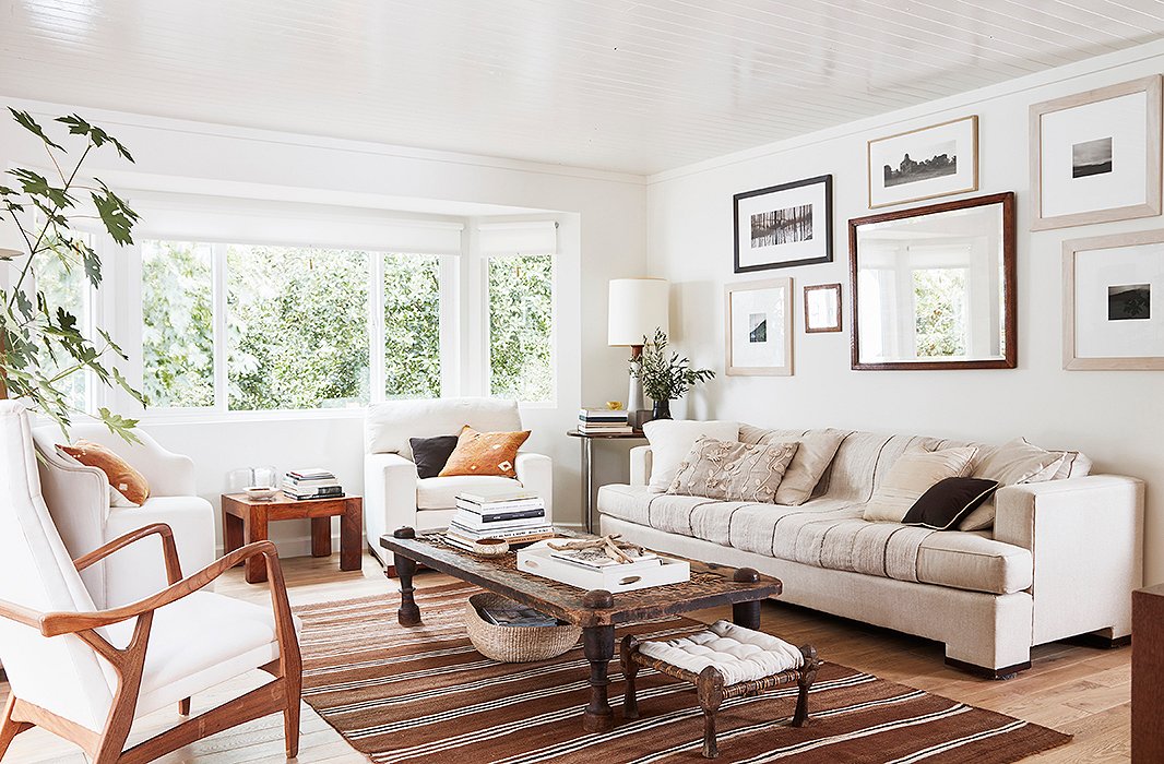 A careful curation of old and new gives the neutral living room vibrancy and life. In the corner, a Scandinavian lamp sits atop a Marcel Breuer table adjacent to an antique beveled mirror and art by Cloud, Laura, and Louis Conner. An antique Nepali daybed functions as the coffee table, mimicking the hues found in the Turkish kilim below. 
