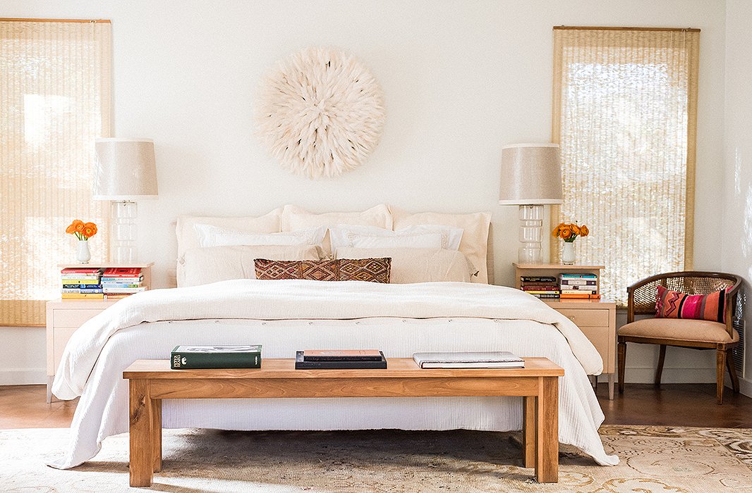 A juju hat flanked by oversize lamps serves as a dreamy focal point in the master bedroom. The wooden bench is an ideal spot to toss throw pillows at bedtime.

