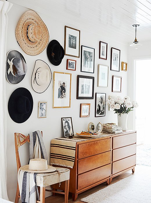 A Navajo runner unites two vintage dressers from Russel Wright beneath a collection of secondhand hats and family photographs. 
