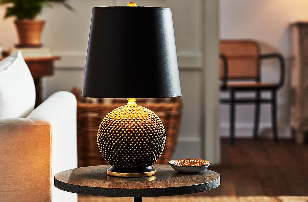 Thanks to its small shape, the Mini Ball Table Lamp (shown here in black with a black shade) is a fitting accent for any space. The details are what really shine on this piece: Gold leaf is hand-applied to the base and every tiny bump, and the shade is lined with a gold finish for an extra luxurious look. 
