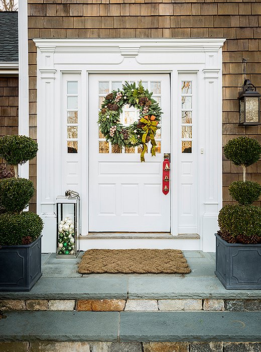 A bow-bedecked wreath and an outdoor lantern filled with ornaments set a festive tone for guests’ arrival. 
