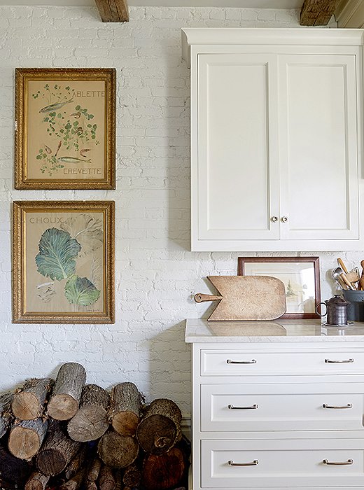 Painted brick and exposed beams add a rustic touch to the up-to-date kitchen designed by Debra Hupman. Firewood, used when temperatures drop, doubles as decor, serendipitously matching the French prints just above. 

