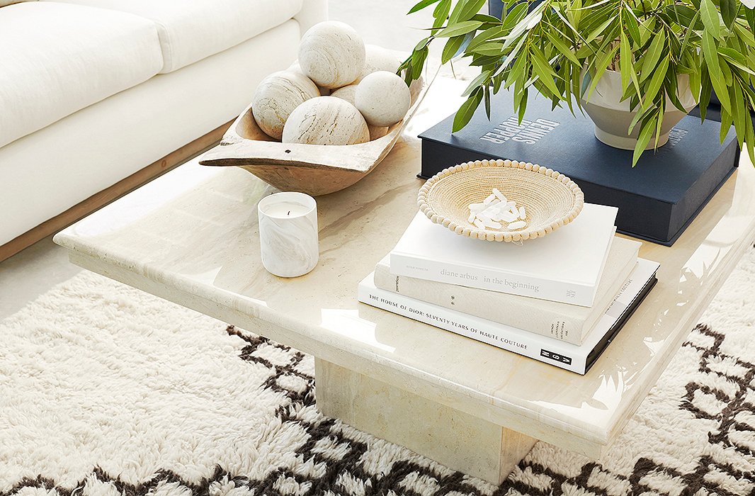 An Italian travertine coffee table from the 1970s brings a sense of polish to the laid-back space. On top, a French dough bowl was filled with a set of spheres selected to match the tone of the table’s stone. 
