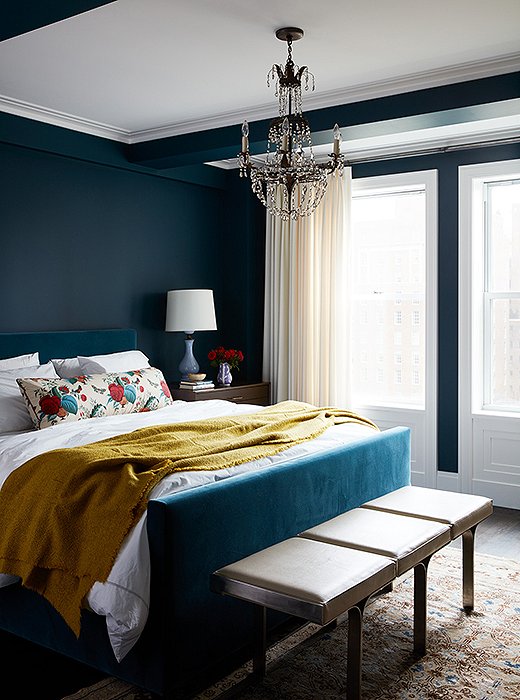 A velvet-upholstered bed blends seamlessly with the peacock-blue walls in the master bedroom.
