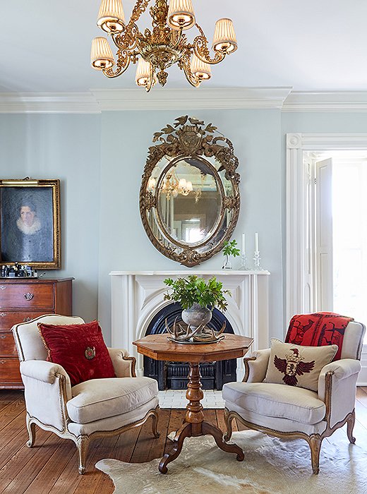 The organic shape of a hide rug provides a contrast to an octagonal table centered to the fireplace and an antique mirror. Bold touches of red, as seen in the crushed-velvet pillow and the cashmere throw, draw the eye toward the architectural focal point just behind. 
