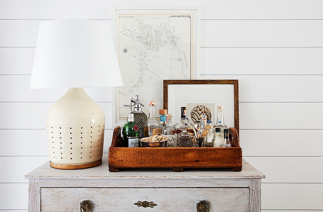 A Ralph Lauren Home lamp sits atop a vintage chest with an oversize tray transformed into a bar. “It’s a move that allows you to take the party wherever it needs to be,” Sally says, and encourages guests to help themselves while you’re busy hosting. A map, picked up by Will on his travels, hangs on the wall behind.
