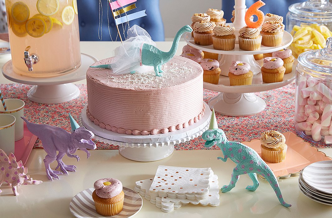 A pretty tablescape comes together quickly with ceramic cake stands and glass jars, which instantly elevate store-bought confections. Toy dinosaurs painted in pastel hues add a playful touch, and striped plates feel festive (and can be used for a grown-up dinner party on another day). 
 
