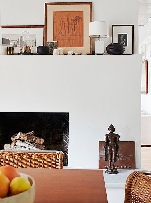 The dining room’s fireplace showcases Laura’s appreciation for modernist design. Functional and void of ornamentation, its mantel hosts wooden Tibetan vessels and a lamp by Aero Studios. On the hearth, a vintage copper printing plate and a bodhisattva lend a sense of calm. 
