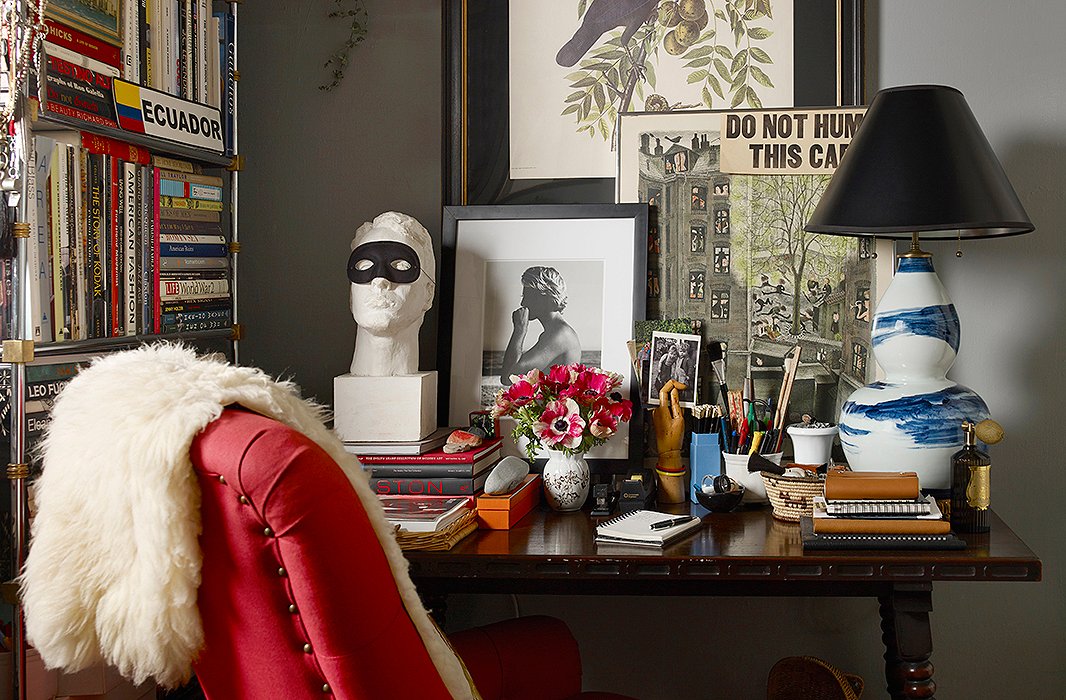 Michael Bastian’s “home office” centers on a spindle-leg table flanked by a masked bust and a Bunny Williams Home lamp. The black-and-white photograph of a lifeguard, a work by photographer Matt Albiani, leans against a wall painted in Glidden’s Ascot Blue.
