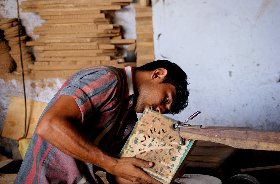 A woodworker perfects a delicately carved pattern. Carved wood is frequently combined with brass and other metals to produce a finished piece. Photo courtesy of Mela Artisans.
 
