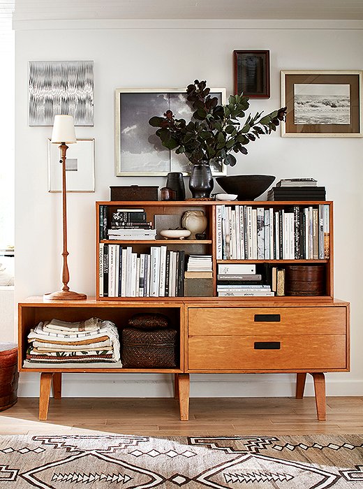 In the foyer, a vintage Danish book cabinet hosts a collection of good reads and sentimental treasures. Placed with asymmetry in mind, the candlestick lamp from Aero Studios guides the eye toward artwork by Alexandra Hedison and Gail Resen (Laura’s mother) and a photograph taken by Laura herself. On the floor, a Navajo blanket was repurposed as a rug, adding warmth, texture, and graphic interest. 
