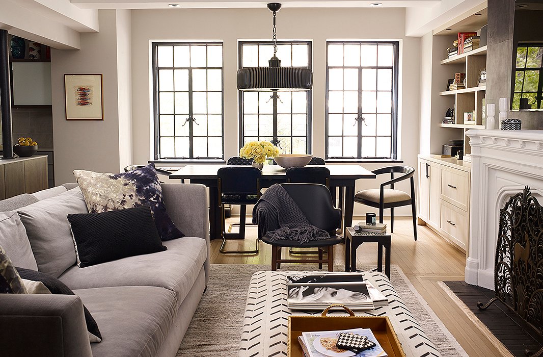 The open-plan living, kitchen, and dining area is flooded with light that pours in from the original iron-frame windows (Suki and Morgan worked with architect Pamela Glazer to transform the apartment from a cramped state to the wide open space it is now). A deep-seated sofa in gray velvet is accented with graphic pillows by Kim Salmela and paired with an ottoman by Tammy Price to create an area perfect for lounging (and the occasional afternoon nap).
