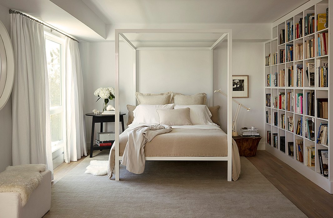 A Tizio lamp separates the canopy bed from a wall of built-ins designed by Foley, with cubbies that make organizing books by category an easy feat. On the floor, a taupe rug bridges the tonal gap between the oak floors and the matte walls (painted in Benjamin Moore’s Decorator White).
