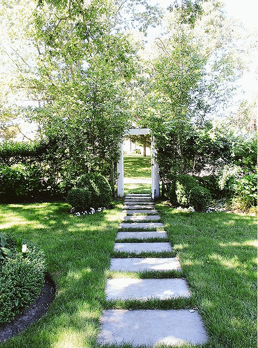 The garden is as charmingly undone as the rest of the home, with boxwood shrubs flanking the entryway and simple stone slabs forming a path through the grass.

