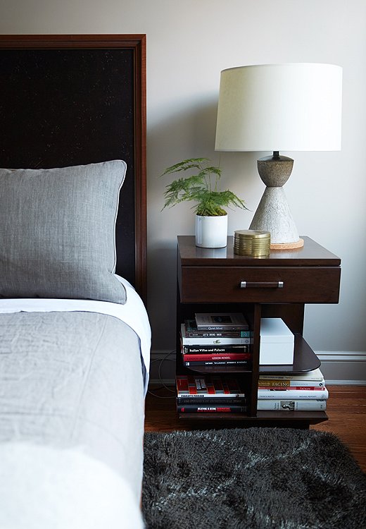 A conical concrete table lamp sits atop a book-filled nightstand with smart open shelves.
