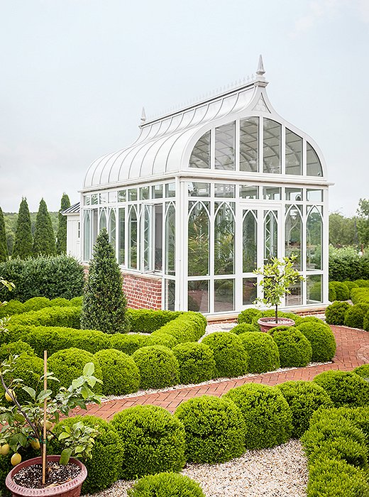 Designed in the shape of a Gothic arch, the greenhouse has smaller arches tracing the glass windows. Boxwood parterres surround the greenhouse, including a row of tall columnar boxwoods that hide the cutting garden in the back.
