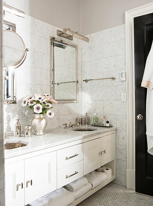 Originally the second-floor kitchen, the master bath was revamped with honed Carrara marble wall tiles, gleaming fixtures, and octagonal sinks, a nod to the home’s architectural elements one floor below. The walls are painted in Benjamin Moore Aura.
