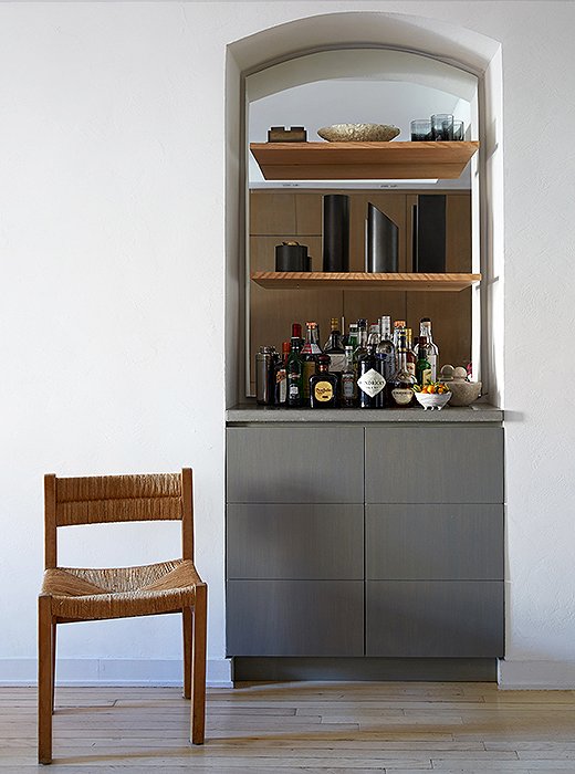 Samuel transformed a bookshelf into an alluring smoky-gray bar by gutting the space and installing a mirror with cove lighting underneath. The lower section is a hideaway spot for television equipment.
