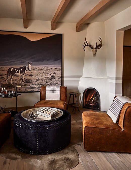 Each room features specific nods to the history of Bishop Lodge. In this guest room, leather chairs and hide rugs add depth, with oversize photography creating a focal point.
