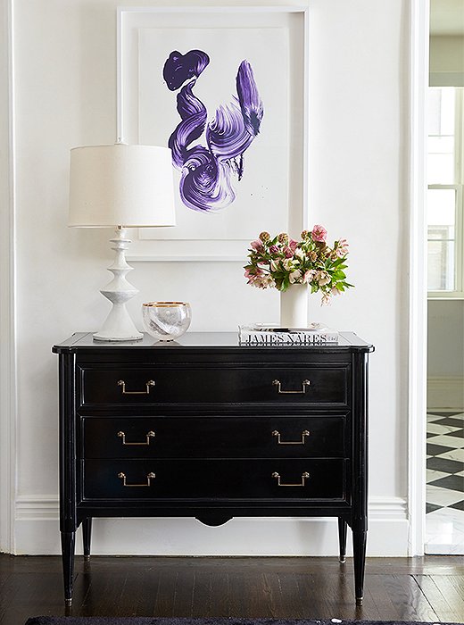 Elsewhere in the entryway stands a black chest topped with a plaster lamp and a rock-crystal bowl. Above, a contemporary stroke of purple by artist James Naras hangs in conversation with the splatter-print area rug below. 
