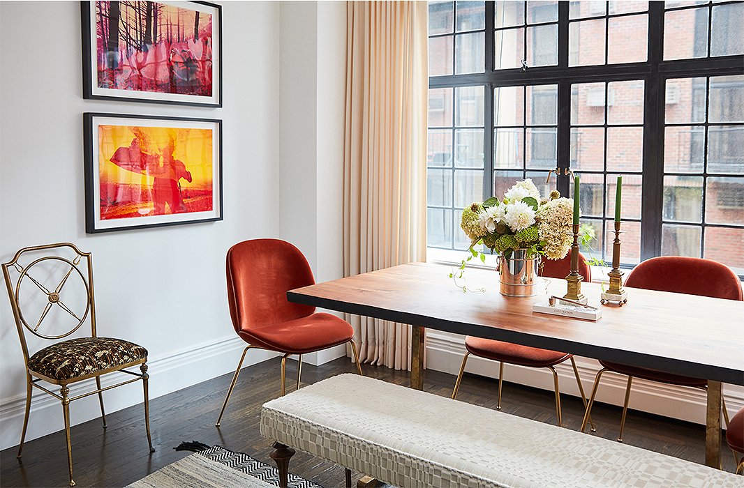 A Marc Bankowsky bench sits on one side of the live-edge dining table, providing ample seating while keeping sight lines open. Contemporary chairs in a rich orange velvet pick up on the warmer tones of the adjacent photographs—and, paired with an ornate brass side chair and classic candlesticks, make for a stylish mix of old meets new. 
