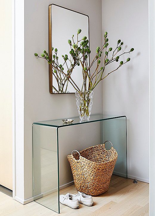 The Franco Wall Mirror sits over a glass waterfall console table in the entry. A woven basket and greenery add natural warmth.
