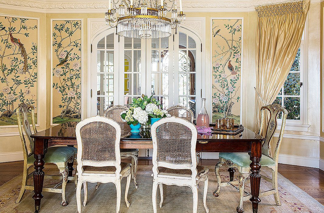 The glossy turquoise flowerpots on the table provide a pop of bright color. Even without them, though, this dining room would be far from monotone, thanks to the fanciful wallpaper panels and the coordinating green velvet upholstery.
