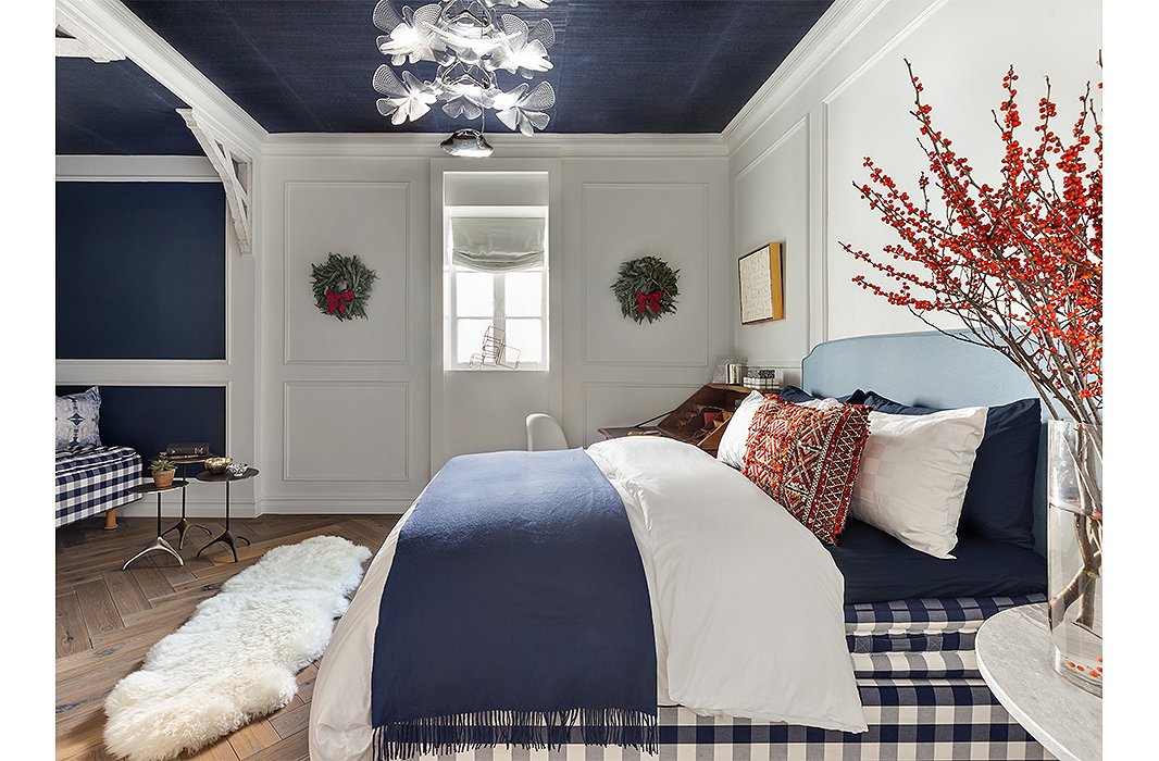 A bedroom by Sara Touijers evokes a Nordic winter with blue-and-white gingham, barn-style trusses, and a sheepskin throw. Wreaths and bittersweet branches play up the holiday theme. Photo by Regan Wood Photography.
