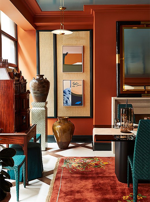 A corner vignette bathed in sunlight boasts colorful contemporary prints, a pedestal, decorative pedestal by Global Views, and sculptural ceramic pots from FEA Home. Custom panels of open cane webbing on the walls lend extra depth and texture to the room. The floor lamp in the corner is by Visual Comfort.

